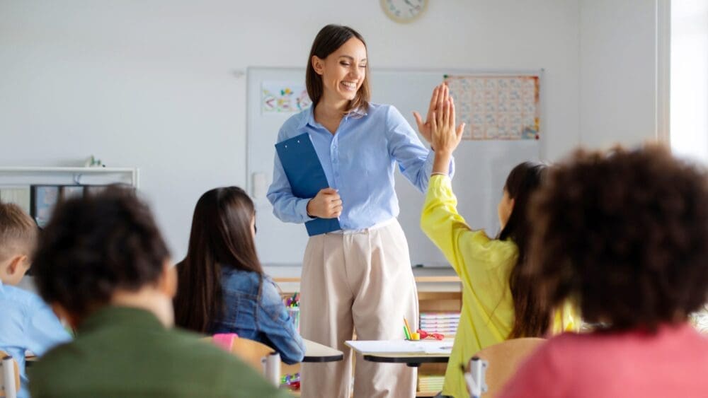 A teacher sitting with a small group of smiling students in a classroom discussion